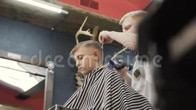 理发店里有客户小孩的理发师。 理发店的理发师使用修剪机和梳子。 可爱的孩子坐在